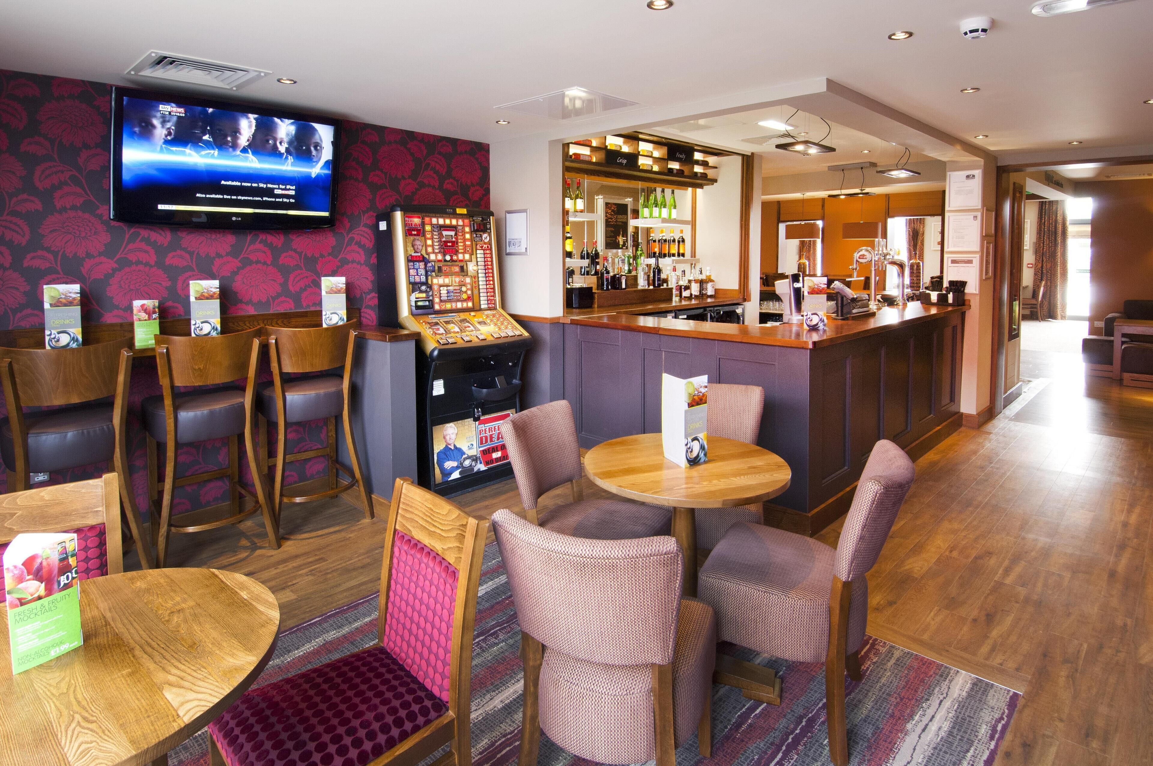 A hotel lobby with a bar area, seating arrangements, a television screen, and a vending machine.