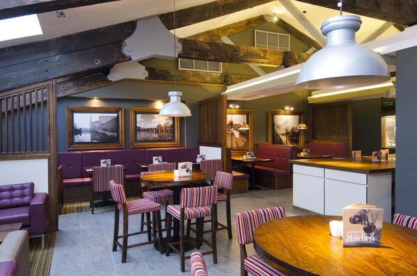 A restaurant with a wooden dining table, striped chairs, and a large pendant light. - Premier Inn Kidderminster (Kidderminster)