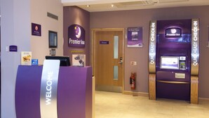 Un espace d’accueil d’hôtel avec une pancarte « BIENVENUE », une enseigne « Premier Inn », une porte marquée « Privé » et un appareil d’enregistrement rapide et facile.
