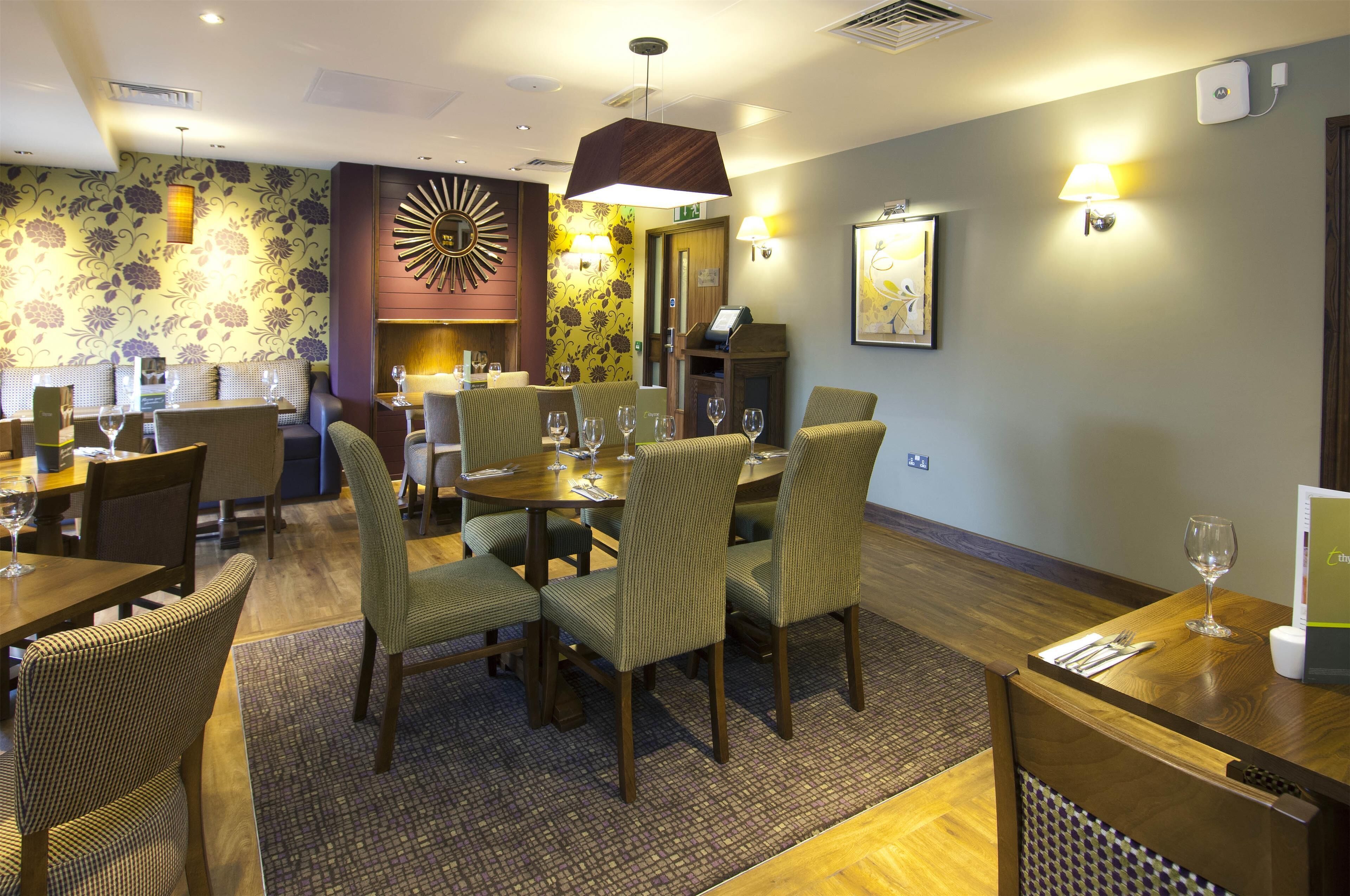 A hotel dining area with multiple tables and chairs, a patterned wall, and a modern chandelier.