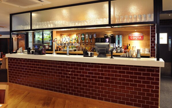 A bar area with a counter, a cash register, and a variety of bottles and glasses. - Premier Inn Redditch North - A441 (Redditch)