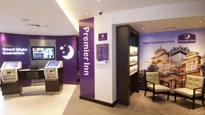 A Premier Inn reception area with a digital screen, a 'Good Night Guarantee' sign, and a 'Welcome to Royal Leamington Spa' poster. - Premier Inn Leamington Spa Town Centre (Royal Leamington Spa)