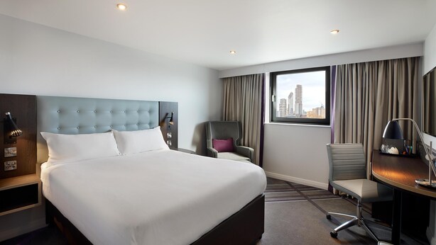 A hotel room with a large bed, a desk, a chair, and a view of the city. - Premier Inn Leamington Spa Town Centre (Royal Leamington Spa)