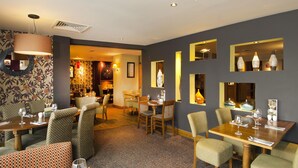 A restaurant with multiple dining tables and chairs, a patterned carpet, and decorative wall mirrors. - Premier Inn Shrewsbury Town Centre (Shrewsbury)