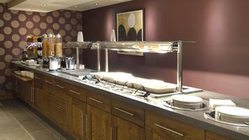 A buffet setup with a variety of food containers, a coffee station, and a counter with plates and napkins.