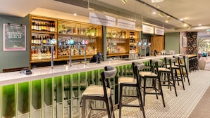 Zona de bar con una barra alargada, taburetes y estanterías llenas de botellas y vasos.