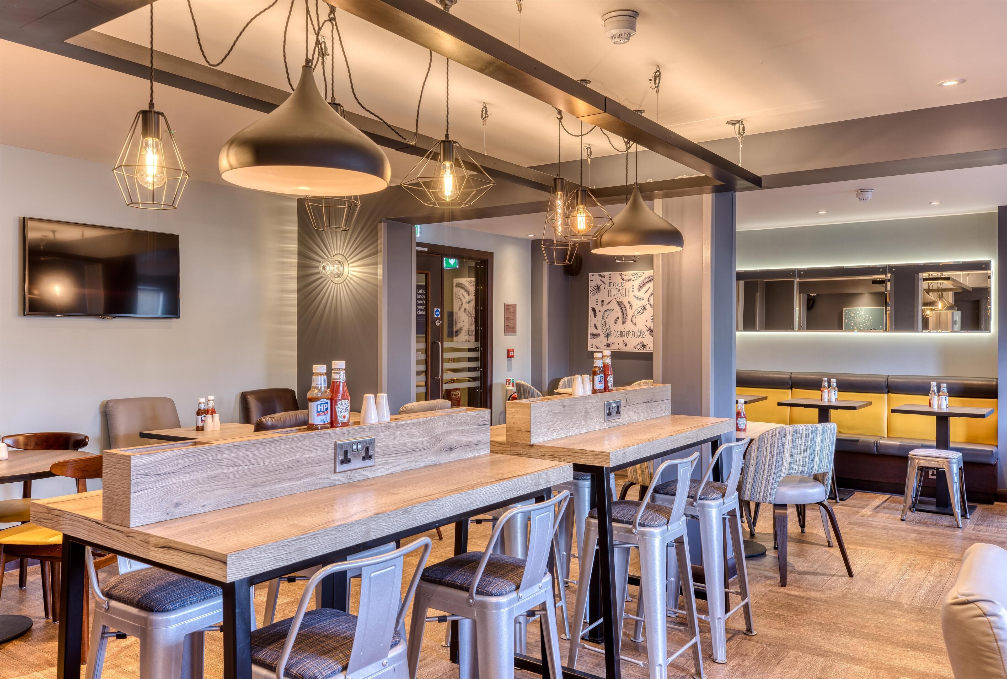 Ein modernes Restaurant-Interieur mit hohen Tischen, Barhocker, Pendelleuchten, einem Flachbildfernseher und einer Theke mit Gewürzen.