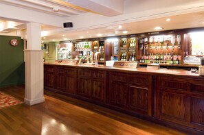 A bar area with wooden cabinets, a counter, and various bottles and glasses. - Premier Inn Christchurch - East (Christchurch)
