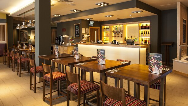 A restaurant with wooden tables and chairs, a bar area, and a menu board. - Premier Inn Dorchester (Dorchester)