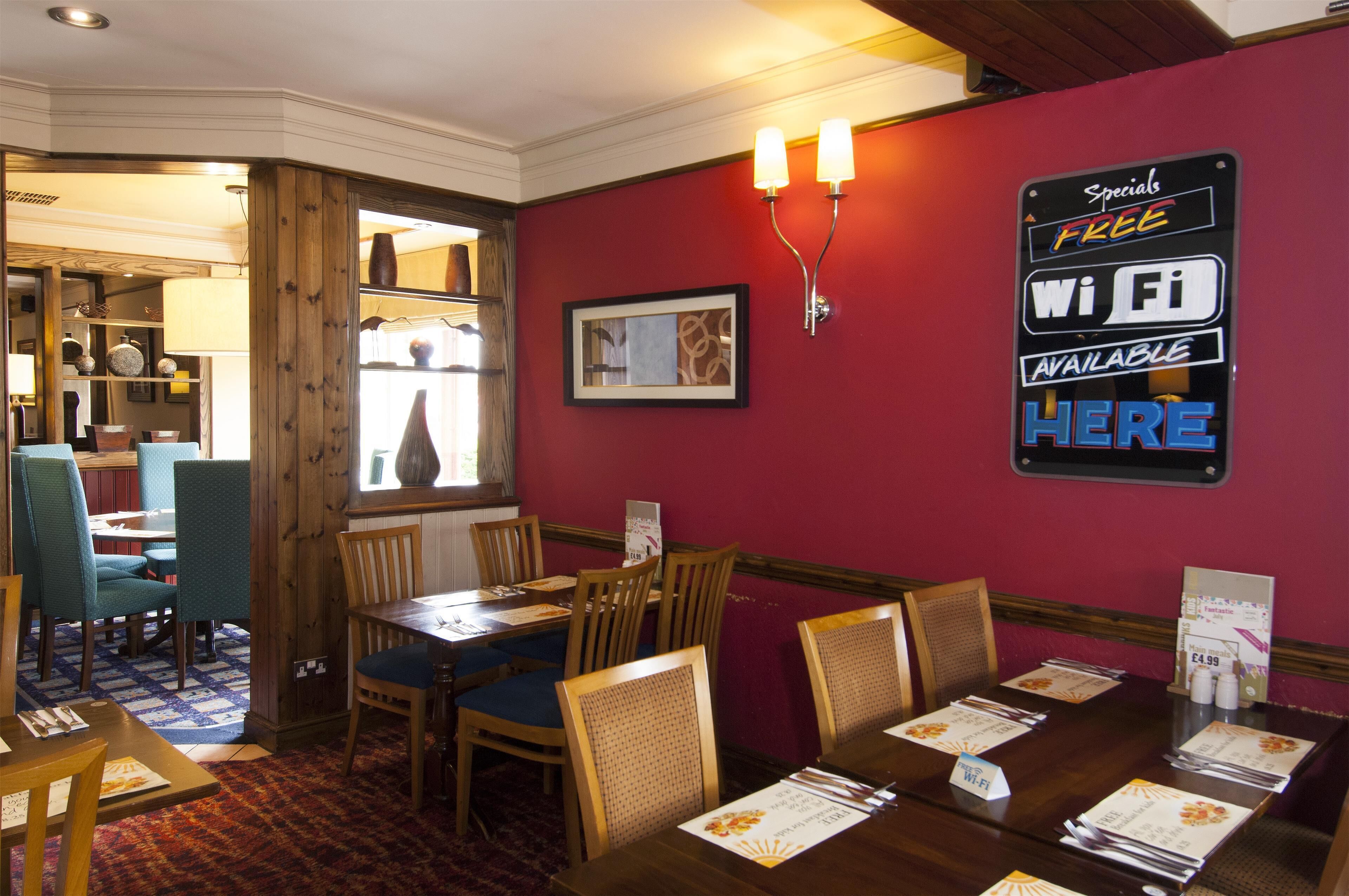 Un comedor con mesas y sillas de madera, una pared roja y un cartel que indica conexión Wi-Fi gratuita.