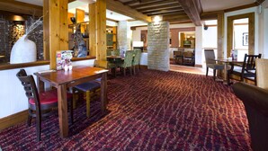 A hotel lobby with a wooden ceiling, stone pillars, a patterned carpet, and a dining area with chairs and tables. - Premier Inn Bristol South (Bristol)