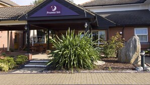 A Premier Inn with a covered entrance, outdoor seating, and a large plant in the foreground. - Premier Inn Bristol South (Bristol)