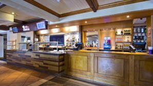 A bar area with a wooden counter, a digital menu display, and a variety of bottles. - Premier Inn Bristol South (Bristol)