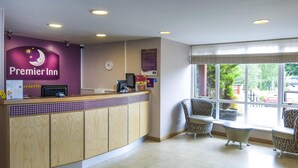A hotel reception area with a counter, chairs, and a view of the outside. - Premier Inn Bradford North - Bingley (Bingley)