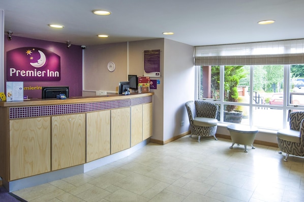 A hotel reception area with a counter, chairs, and a view of the outside. - Premier Inn Bradford North - Bingley (Bingley)