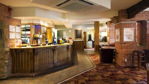 A bar area with a wooden counter, a brick wall, and a patterned carpet. - Premier Inn Bradford North - Bingley (Bingley)