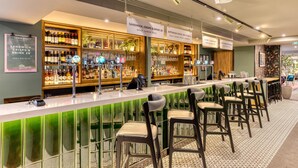 Un espace bar doté d’un long comptoir, de tabourets et d’étagères remplies de bouteilles et de verres.