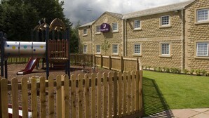 A playground with a slide and climbing structures, a wooden fence, and a building with a sign for Premier Inn. - Premier Inn Skipton North - Gargrave (Skipton)
