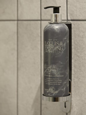 Una botella de Baylis & Harding Elements con dosificador bomba, colocada sobre un muro de azulejos.