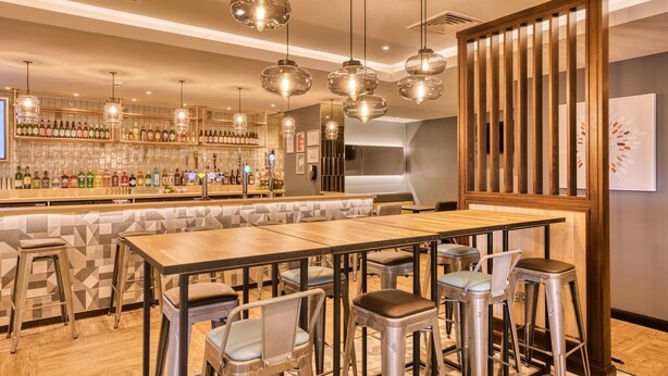A bar area with stools, a long counter, and hanging pendant lights. - Premier Inn Bristol Cribbs Causeway - M5 J17 (Bristol)
