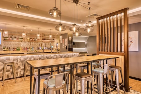 A bar area with stools, a long counter, and hanging pendant lights.. Premier Inn Bristol Cribbs Causeway - M5 J17