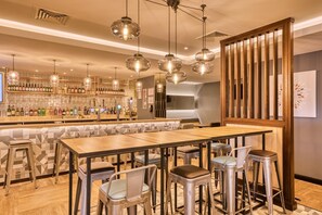 A bar area with stools, a long counter, and hanging pendant lights. - Premier Inn Bristol Cribbs Causeway - M5 J17 (Bristol)
