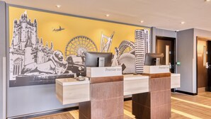 A hotel reception desk with a cityscape mural in the background, a wooden reception desk, and a sign indicating 'Premier Inn'. - Premier Inn Bristol Cribbs Causeway - M5 J17 (Bristol)