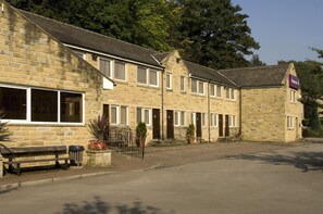 A stone building with multiple windows and doors, a bench, and a trash bin. - Premier Inn Halifax South (Halifax)