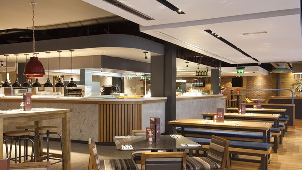A restaurant with wooden tables and benches, a bar area, and hanging pendant lights. - Premier Inn Halifax Town Centre (Halifax)