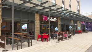An outdoor seating area with tables and chairs, a glass canopy, and a building with a sign that reads 'Beefeater.' - Premier Inn Halifax Town Centre (Halifax)