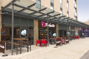 Un espace extérieur aménagé avec des tables et des chaises, un auvent en verre et un bâtiment sur lequel on peut lire l’inscription « Beefeater ».
