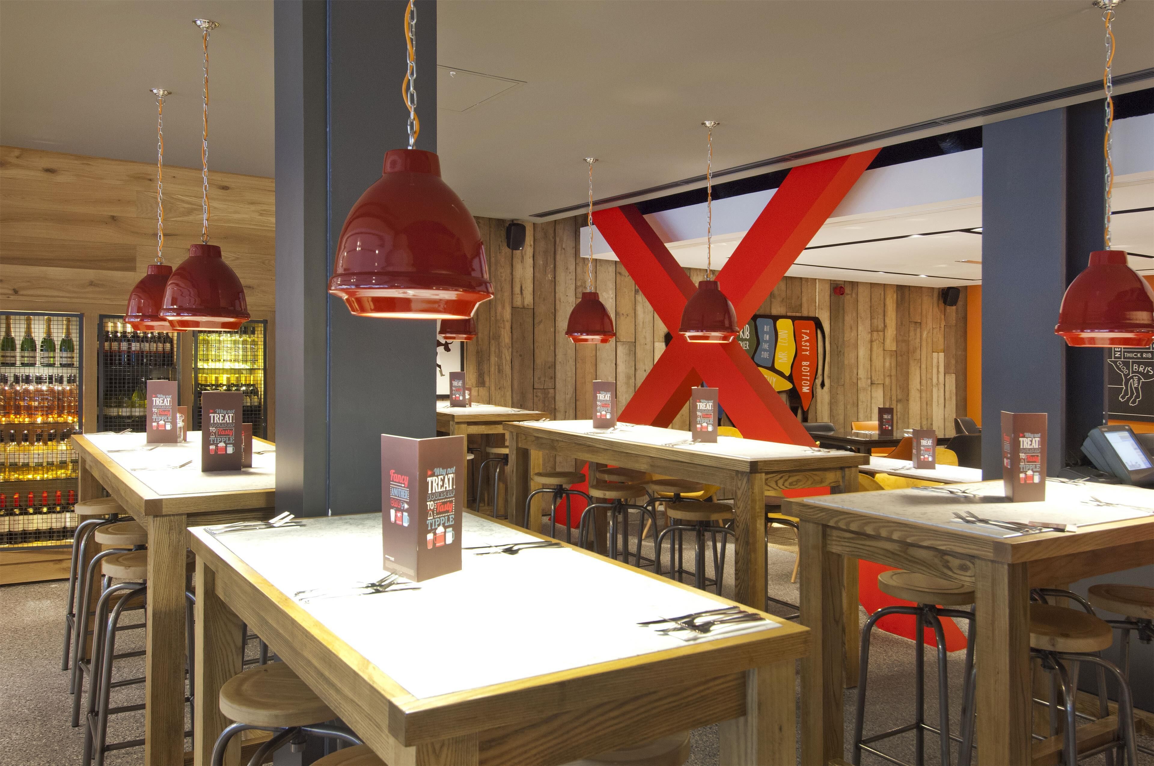 A restaurant interior with wooden tables, red pendant lights, and a large red 'X' on the wall.