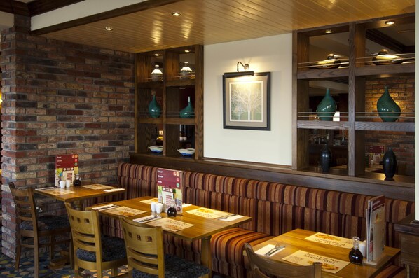 Un restaurante con paredes de ladrillo, mesas de madera, cabinas acolchadas e lámparas colgantes.