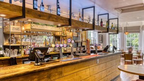 A bar with wooden shelves, a cash register, and various bottles. - Premier Inn Arundel (Arundel)