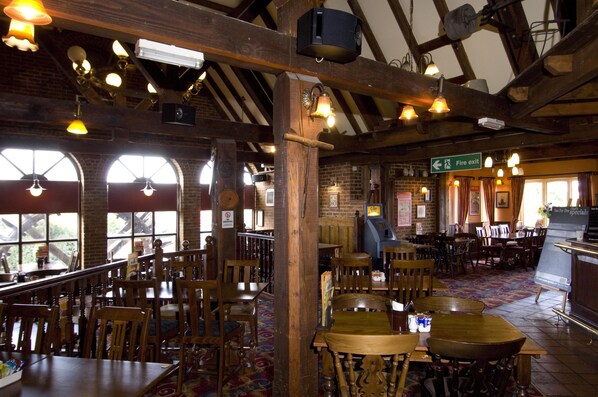 A restaurant with wooden tables and chairs, a fire exit sign, and a view of the outdoors through large windows. - Premier Inn Eastbourne (Eastbourne)