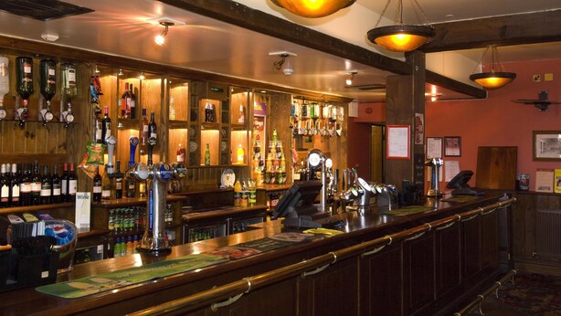 A bar with a wooden counter, multiple bottles, and a cash register. - Premier Inn Eastbourne (Eastbourne)