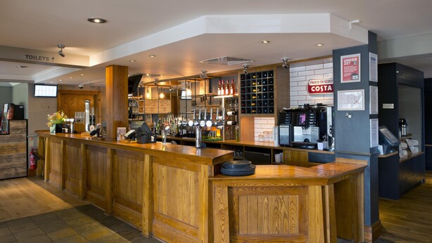 A bar area with a wooden counter, multiple taps, and a wine rack. - Premier Inn Frome (Frome)
