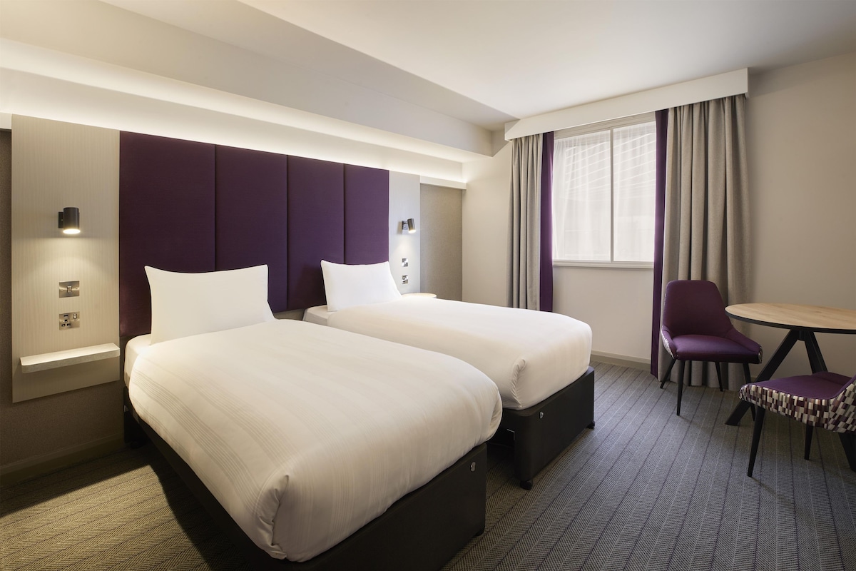 A hotel room with two beds, a desk, a chair, and a window with curtains.