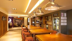 A restaurant with long wooden tables and striped chairs, a bar area, and a sign for 'The Kitchen at Trowbridge.' - Premier Inn Trowbridge (Trowbridge)