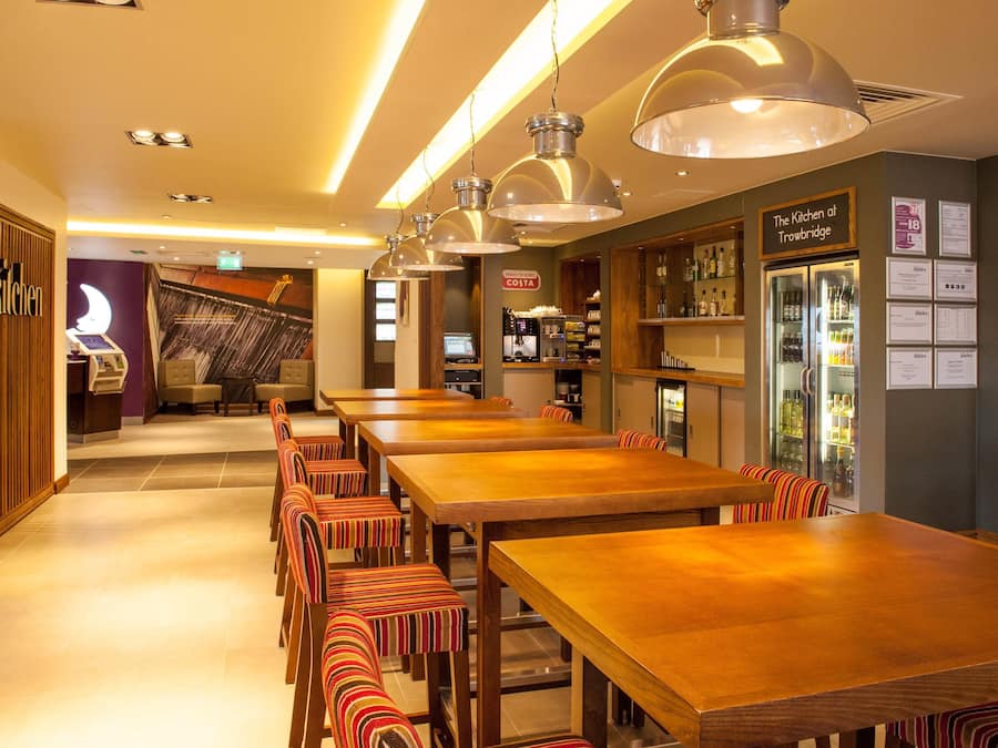 A restaurant with long wooden tables and striped chairs, a bar area, and a sign for 'The Kitchen at Trowbridge.'