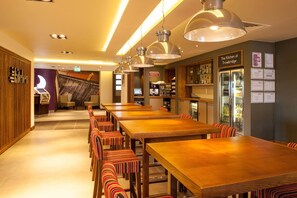 A restaurant with long wooden tables and striped chairs, a bar area, and a sign for 'The Kitchen at Trowbridge.'