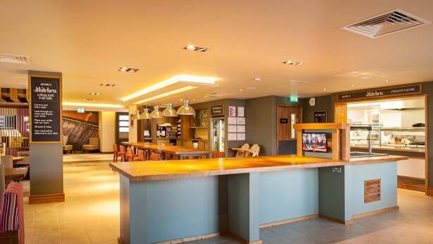 A modern kitchen area with a central island, bar seating, and a dining area with tables and chairs. - Premier Inn Trowbridge (Trowbridge)