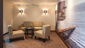 A hotel room with a seating area featuring two sofas and two armchairs, a small round table, and a large wall mural of a pier extending into the sea. - Premier Inn Barrow-In-Furness (Barrow-in-Furness)