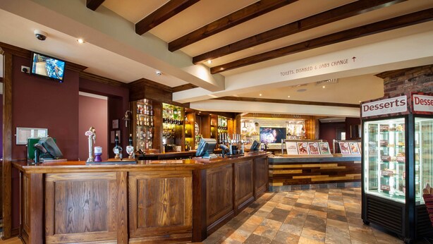 A bar area with wooden counters, a television, and a sign indicating amenities like toilets, disabled access, and a baby change. - Premier Inn Barrow-In-Furness (Barrow-in-Furness)