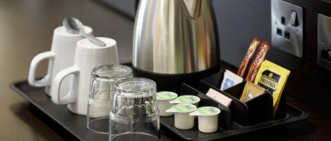 A tray with a kettle, cups, glasses, and packaged snacks.