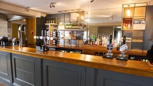 A bar area with a wooden counter, multiple taps, and shelves stocked with bottles and glasses. - Premier Inn Carlisle - M6 Jct42 (Carlisle)