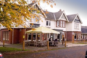 A building with a sign reading 'Border Gate,' featuring outdoor seating with tables and chairs, and a yellow umbrella. - Premier Inn Carlisle - M6 Jct42 (Carlisle)