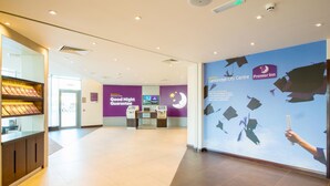 Un hall de hotel con un letrero de 'Garantía de Buenas Noches', el logotipo de Premier Inn y una pared con motivos de birretes de graduación.