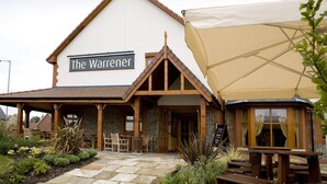 Ein Gebäude namens 'The Warrener' mit einer Steinauffahrt, Holzbalkonen und einer überdachten Terrasse.
