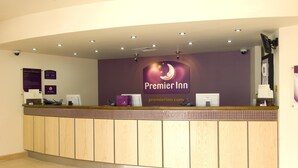 A hotel reception desk with a sign for Premier Inn, a computer, and a security camera. - Premier Inn Cambridge - A14 J32 (Cambridge)